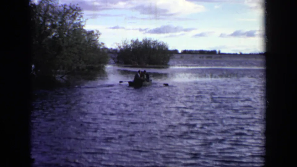 Several people appear in a small rowboat on a Moscow lake, framed by trees and dark 8mm film edges.