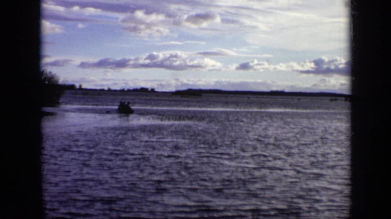 Small boat crossing a wide river beneath a partly cloudy sky.