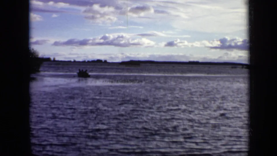 A small boat appears on the river in Moscow, filmed from a shaded bank on 8mm in 1971.