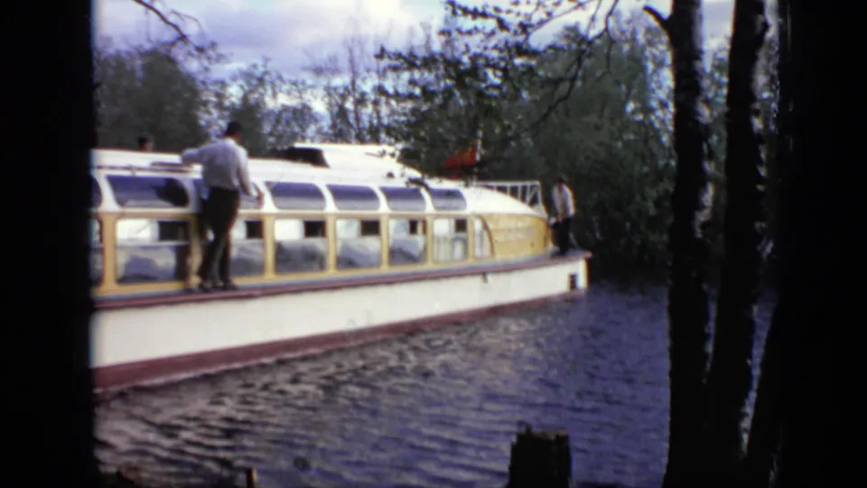 A white and yellow passenger boat passes the riverbank in Moscow with a man visible on deck.