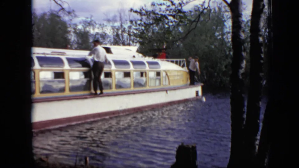 In Moscow home-movie footage from 1971, a man stands on the roof of a white and yellow canal boat as it moves along a wooded waterway.