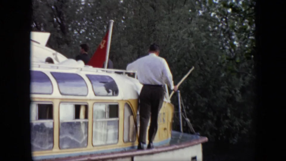 A man stands on the roof of the canal boat with a pole, while a red Soviet flag is visible behind him in the 1971 Moscow footage.