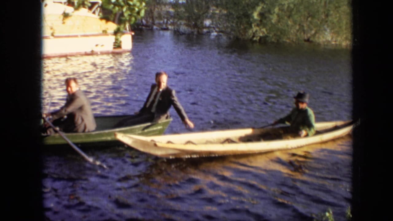 Two men in a green rowboat pass near a pale canoe with another man paddling.