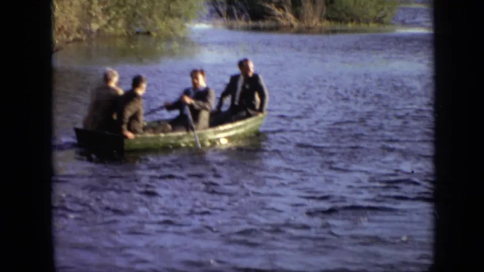 1971 Moscow home-movie frame showing four people in a green rowboat close to shore on rippled water.