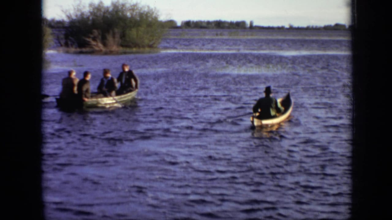 A rowboat with four people moves across open water beside a separate small canoe.