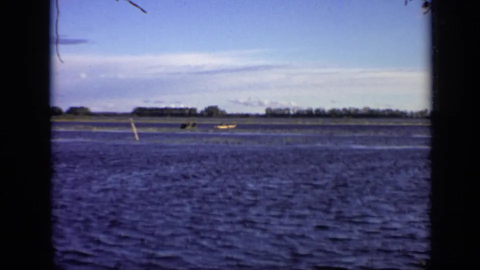 1971 Moscow 8mm frame showing a wide river with small distant boats, reeds or grasses, a low tree line, and visible film gate edges.