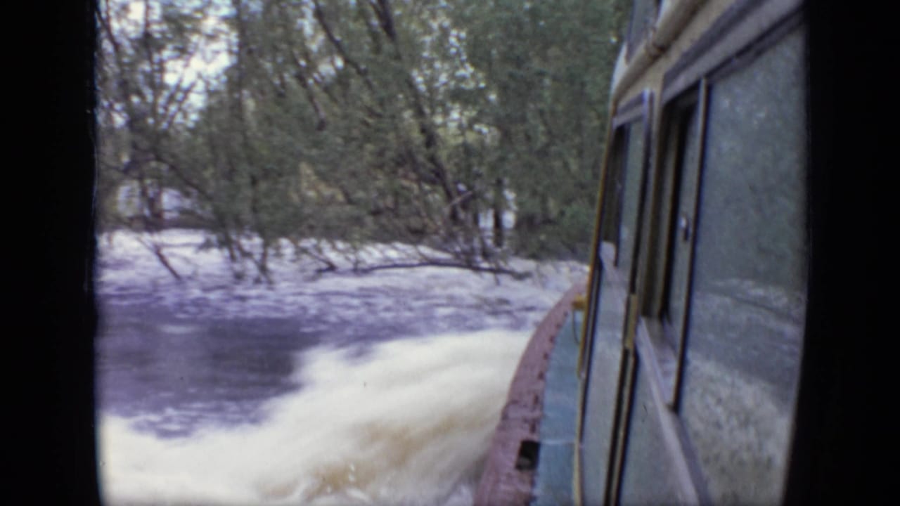 Moving-boat view in the Moscow 1971 home movie, showing pale spray, dark water, and a tree-lined bank.