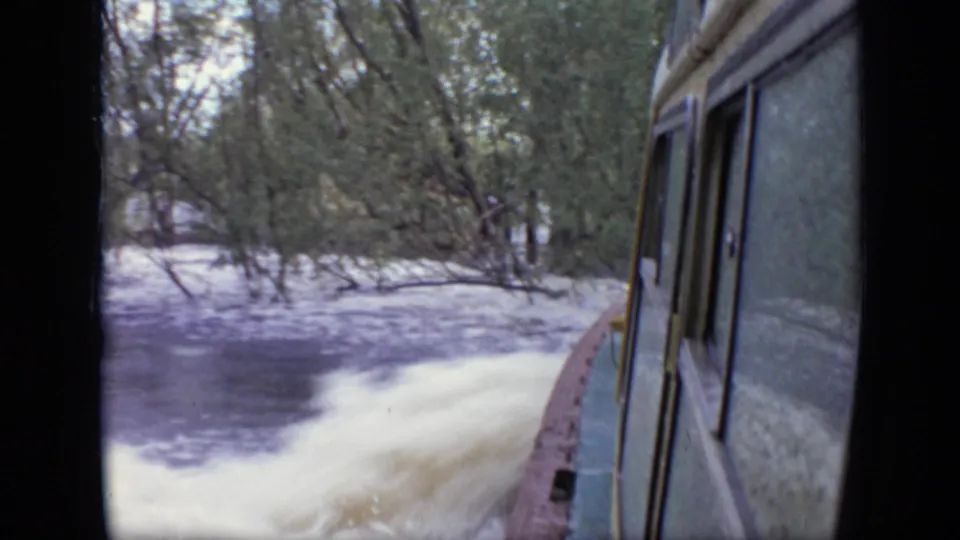 Moving-boat view in the Moscow 1971 home movie, showing pale spray, dark water, and a tree-lined bank.
