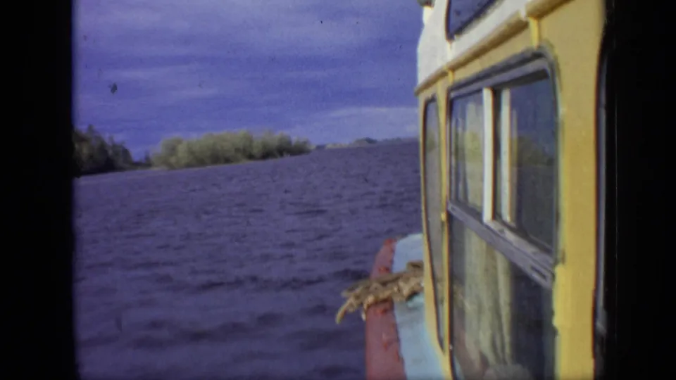 1971 Moscow water-travel frame showing a yellow cabin boat edge, open lake water, distant trees, and cloudy sky.
