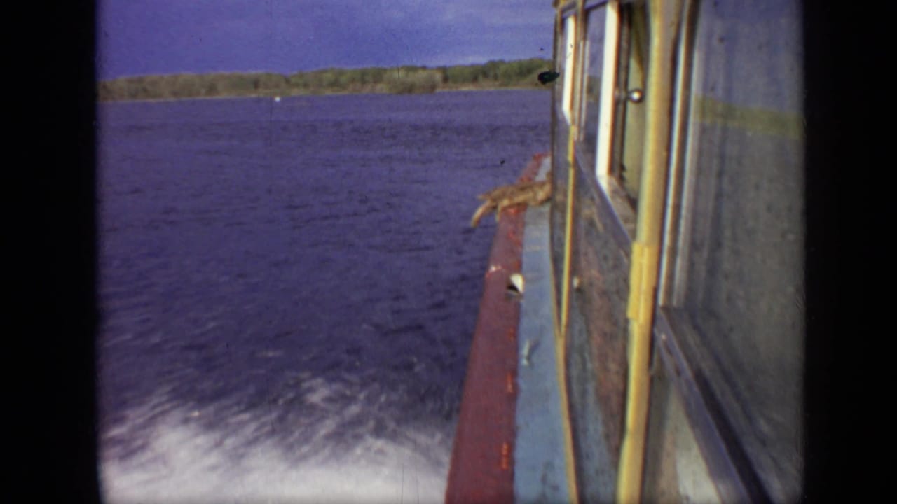 Boat side and cabin windows passing over blue water with a white wake and distant shoreline.