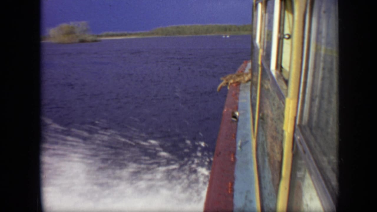 Onboard 8mm view of a boat moving quickly over water near Moscow, with spray behind the hull and a low tree-lined shore in the distance.