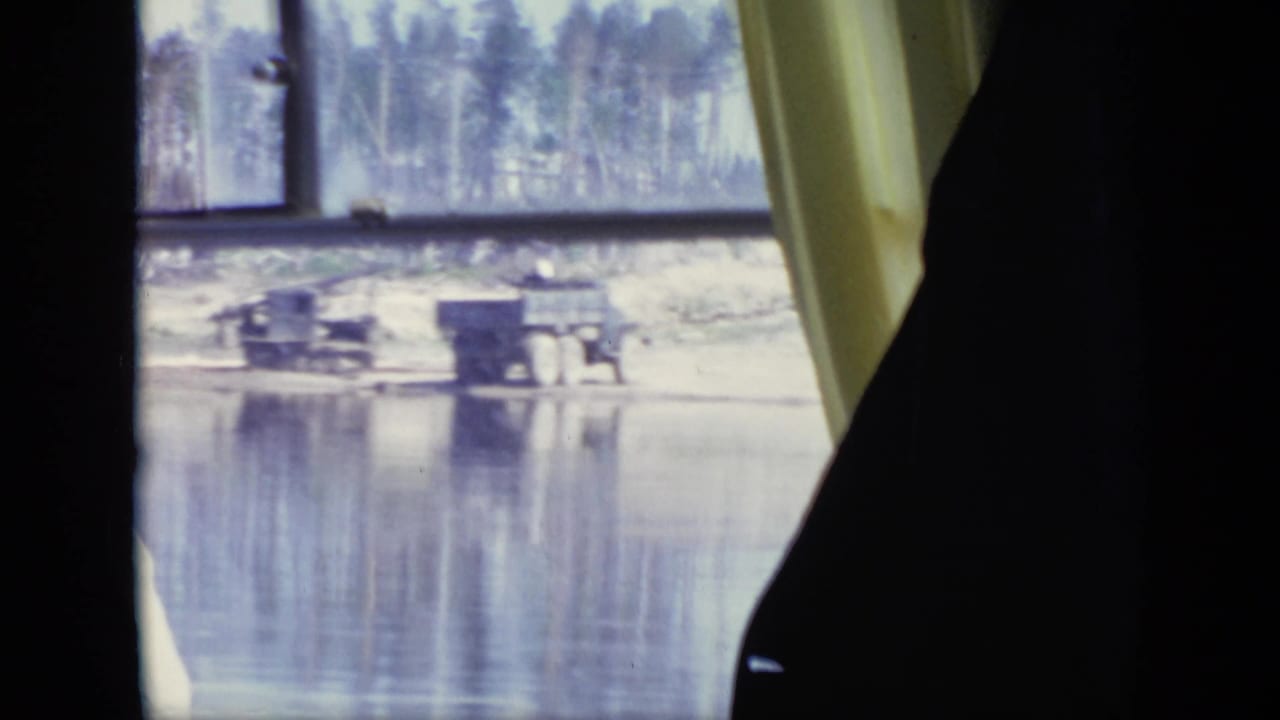 1971 Moscow view through a vehicle window toward a muddy riverside with sparse trees and small waterside structures.