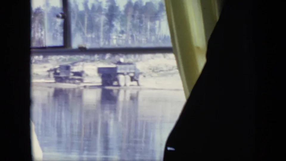 1971 Moscow view through a vehicle window toward a muddy riverside with sparse trees and small waterside structures.