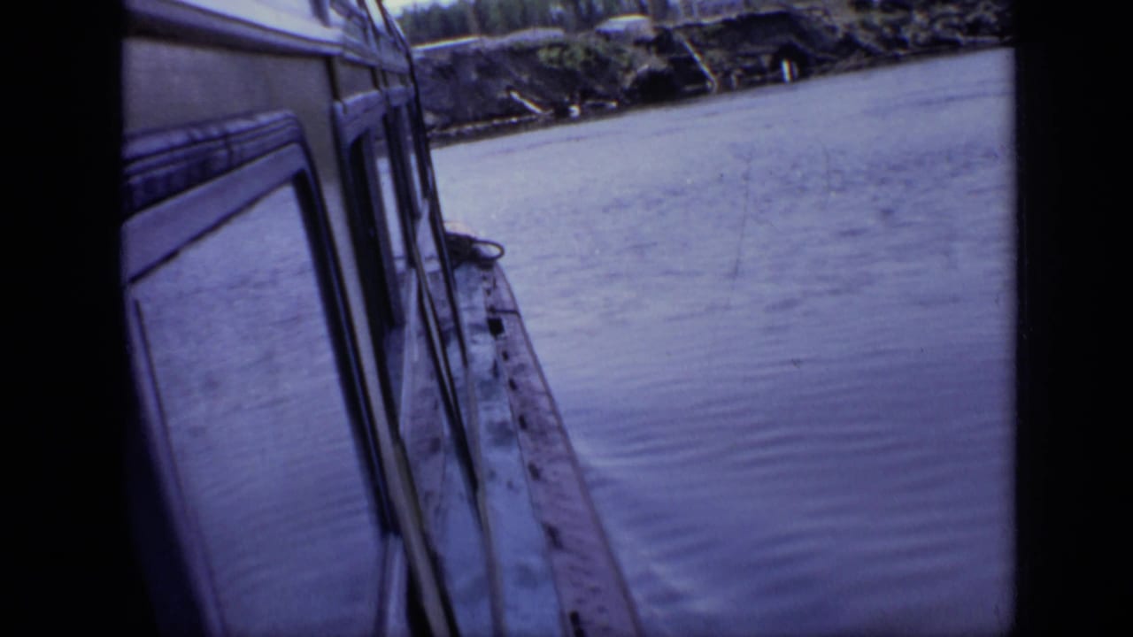 Close side view of a white boat beside calm river water with dark film borders.