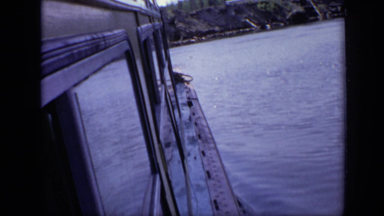 Close angled view along a white boat hull on river water with shoreline in the distance.
