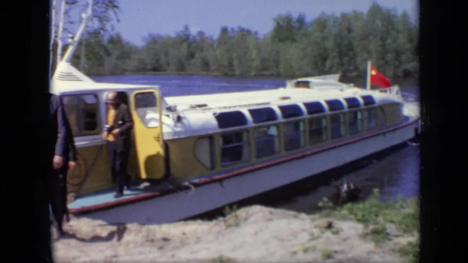 1971 Moscow 8mm frame showing passengers by the open doorway of a white river boat at the shore, with a red flag visible.