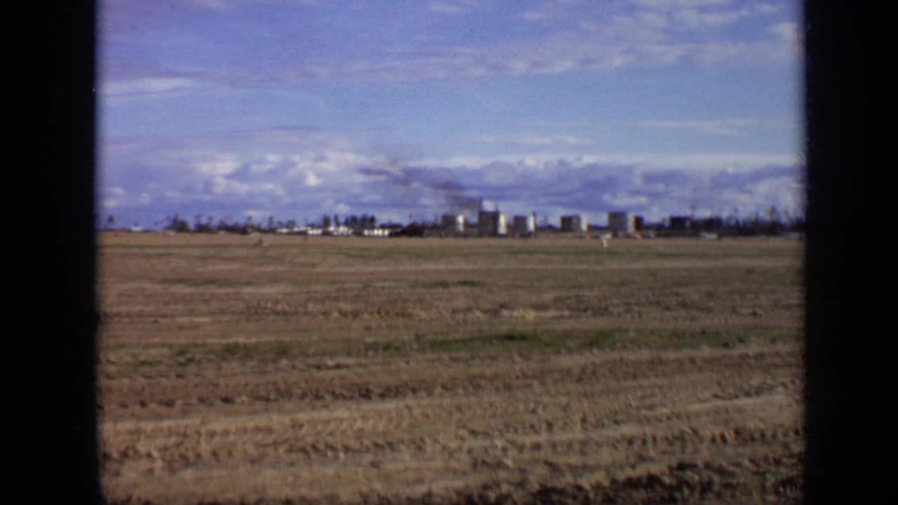 Wide 1971 8mm view near Moscow showing open ground and a distant industrial site with smoke against a blue sky.