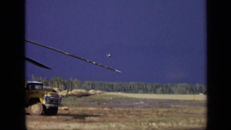 1971 8mm frame near Moscow with a yellow truck partly visible beside open ground, a treeline, and deep blue sky.