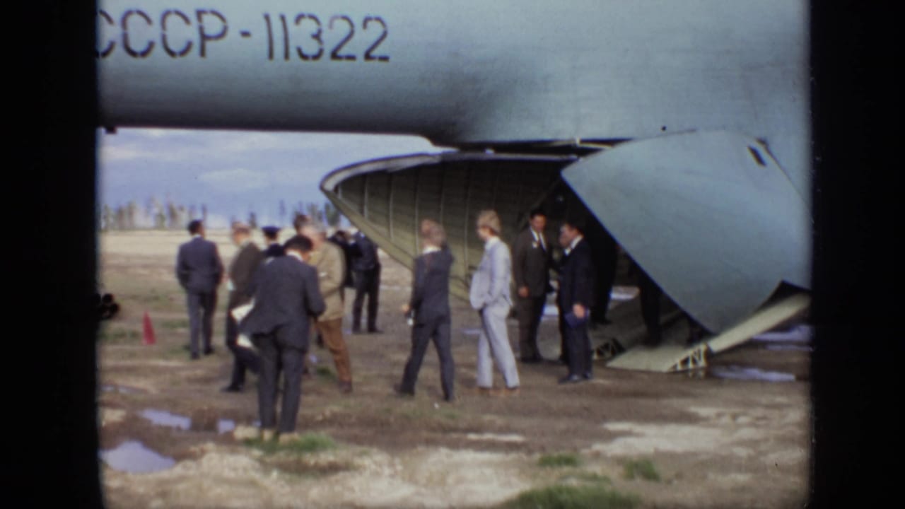 Men gather near the open rear ramp of a Soviet transport aircraft on a muddy airfield.