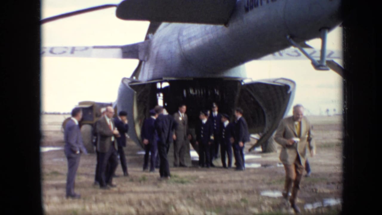 Group of suited and uniformed men stands near the open cargo bay of a transport aircraft.