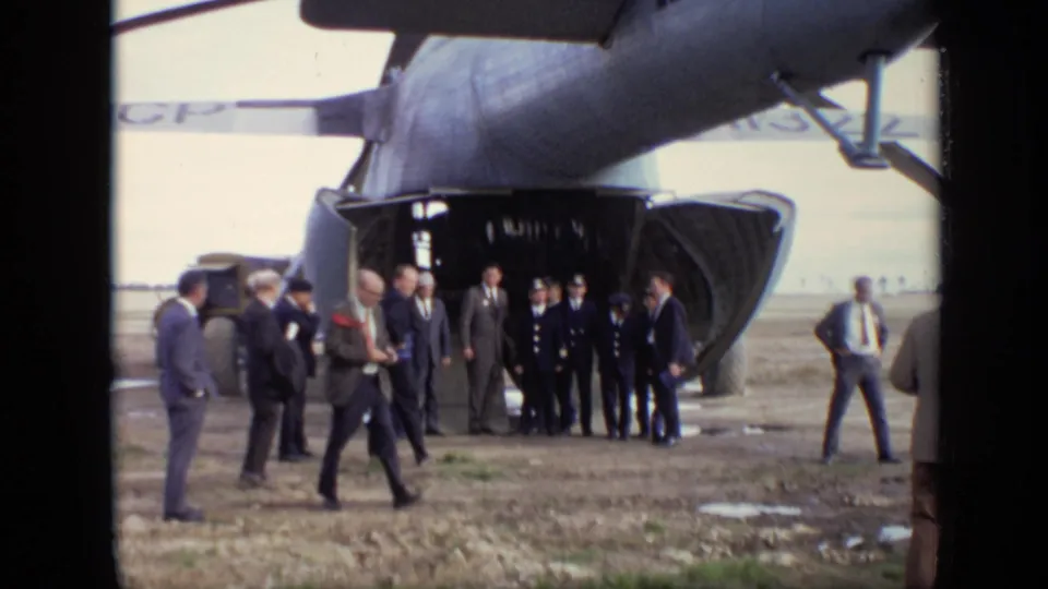 Handheld 8mm view of suited men and uniformed personnel moving near a Soviet aircraft's lowered rear ramp in 1971 Moscow.