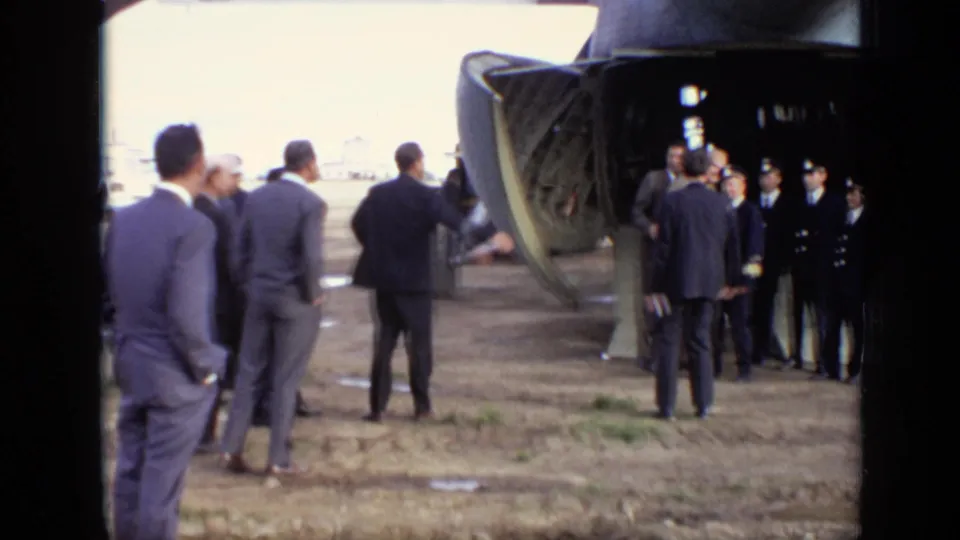 Men in civilian suits and military-style uniforms converse at the rear of an open transport aircraft on a Moscow airfield in 1971.