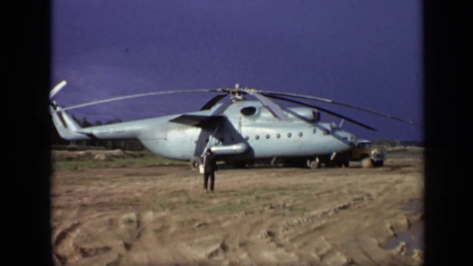 1971 Moscow 8mm frame showing the man closer to the landed military-style helicopter on a rough open field.