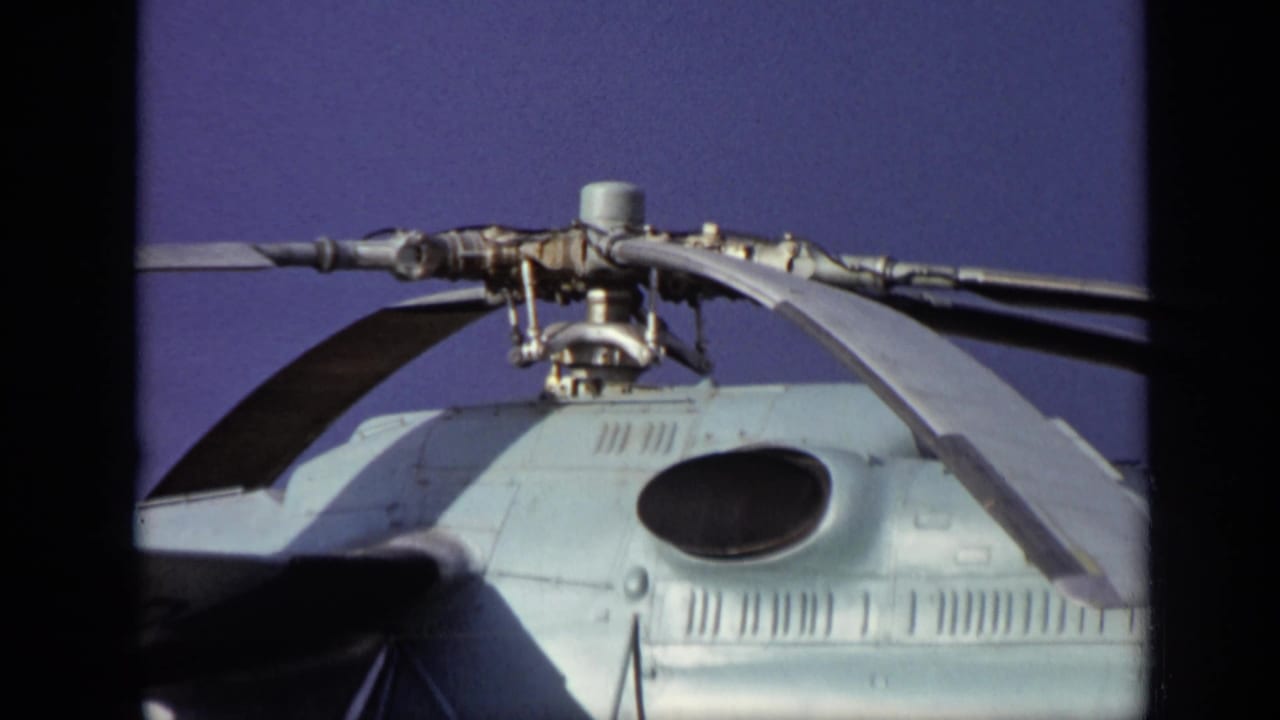 Close view of a helicopter rotor assembly and upper fuselage against blue sky.