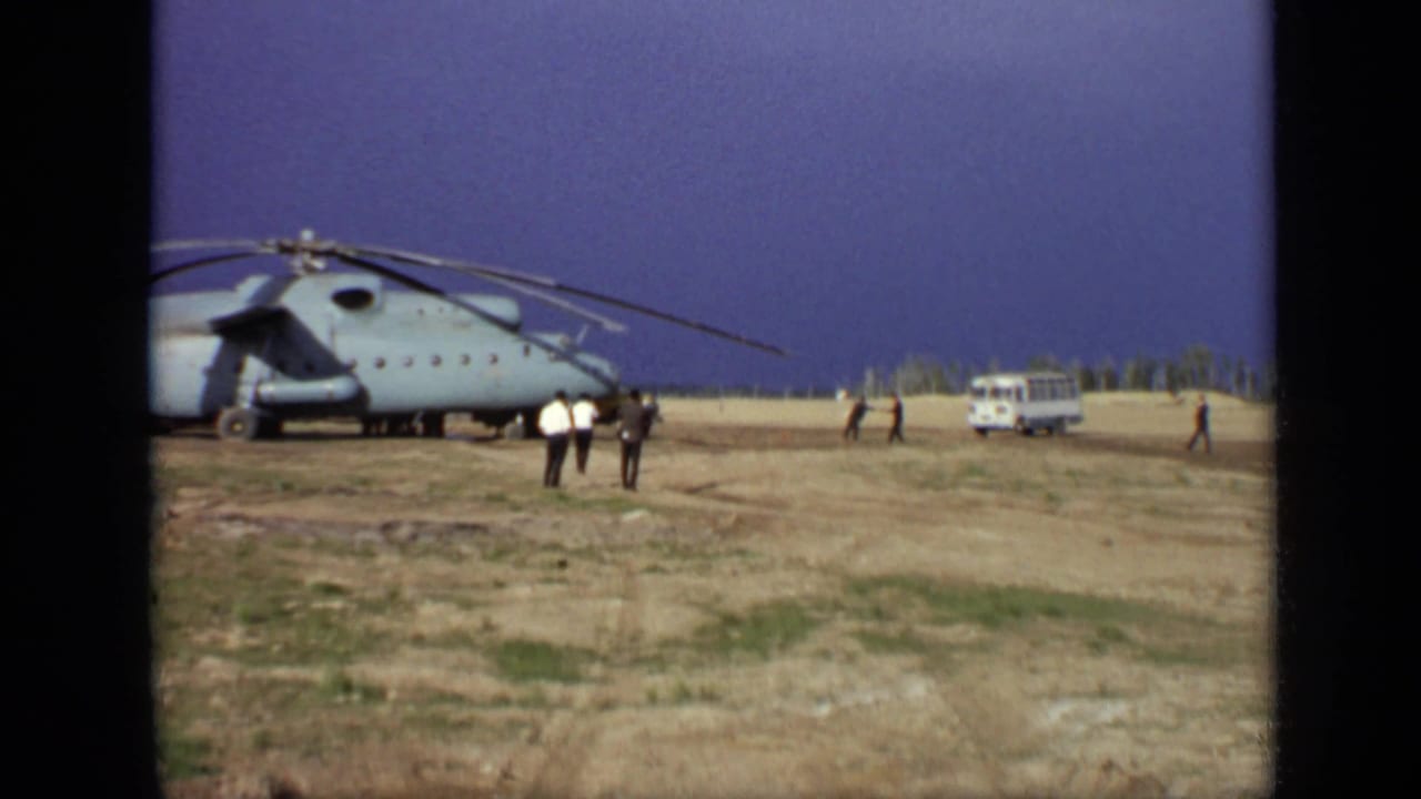 Large helicopter parked on an open field with people and a white van nearby.