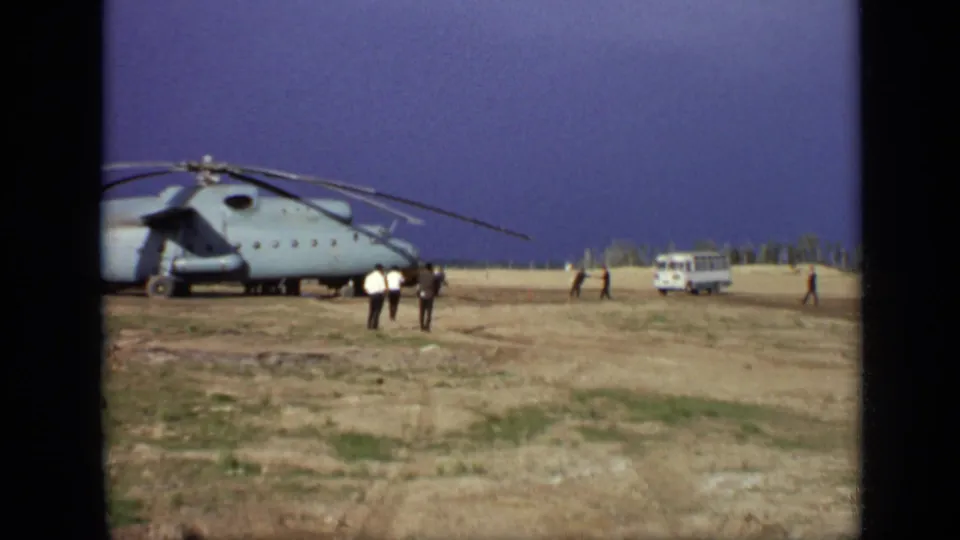 1971 Moscow field view with a large blue-gray helicopter, several adults walking nearby, and a white van in the distance.