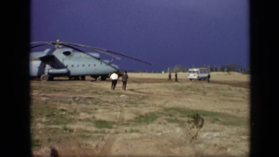 Final 1971 Moscow frame showing the helicopter in profile on an open field, with adults nearby and a white van near the tree line.