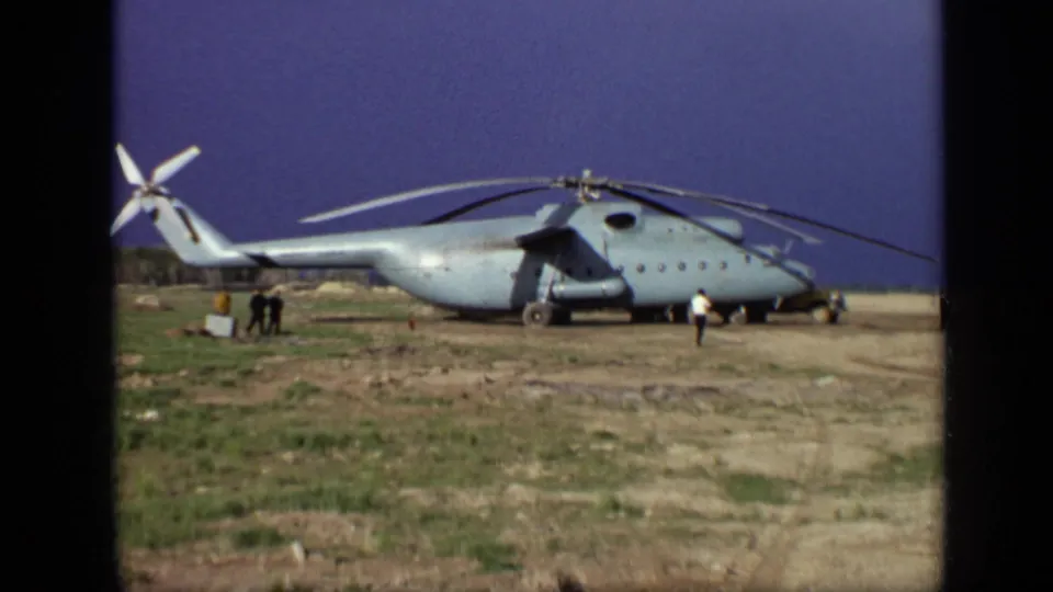1971 Moscow frame of a large military-style helicopter on rough ground, with small groups of people near the tail and nose.