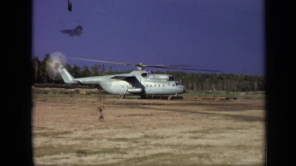 1971 8mm frame showing the helicopter still on the field near Moscow, with visible film dust and a forested horizon behind the aircraft.