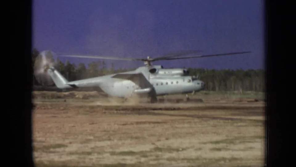 1971 Moscow 8mm frame capturing rotor wash lifting dust around a large helicopter against trees and blue sky.