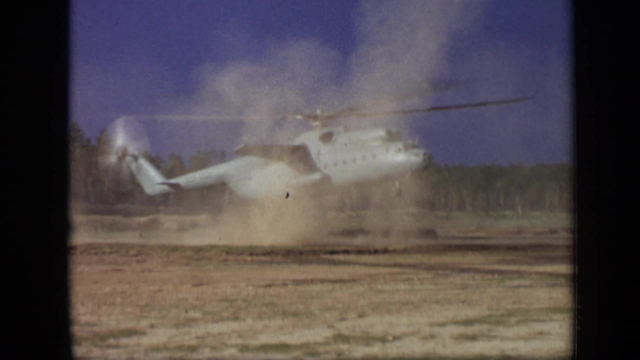 Helicopter rising above the field as a larger dust cloud forms beneath it.