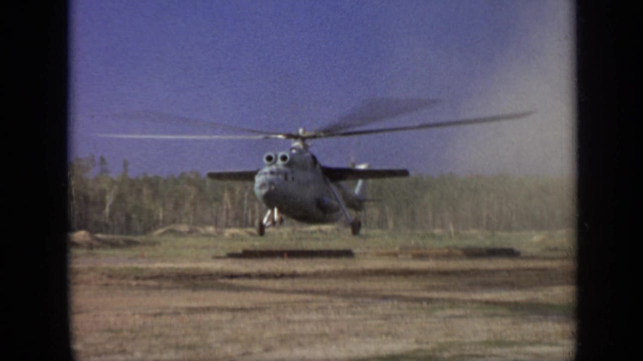 1971 Moscow-area 8mm frame of a military-style helicopter holding a low hover over a dusty clearing near trees.