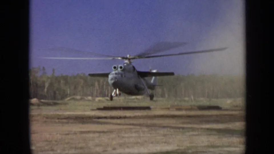1971 Moscow-area 8mm frame of a military-style helicopter holding a low hover over a dusty clearing near trees.