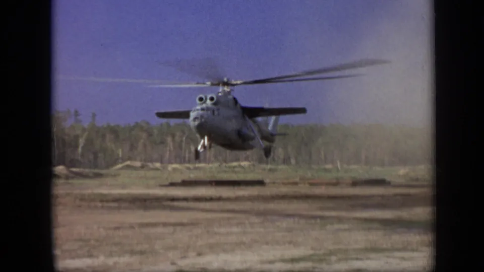 1971 Moscow-area 8mm frame showing the helicopter centered in a low hover, its rotor blurred above a dusty open field.