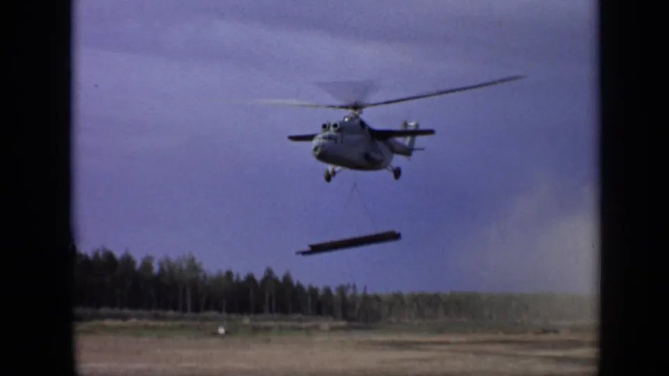 Final frame shows the helicopter carrying the beam over a rural Moscow-area field, with faded 8mm color and visible borders.