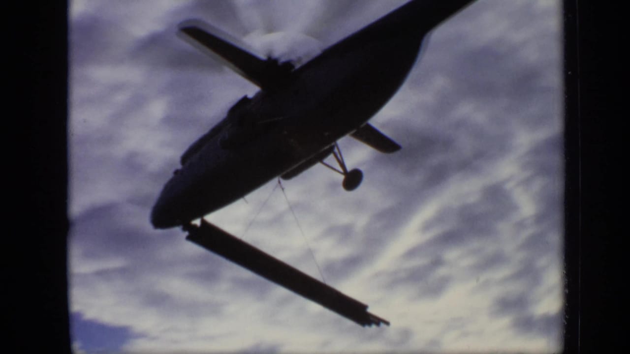 Low-angle 1971 Moscow frame of a military-style helicopter silhouetted against clouds while carrying a steel beam.