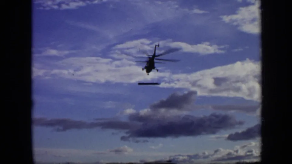 Wide 1971 Moscow frame with a distant helicopter and suspended steel beam crossing a cloudy sky.