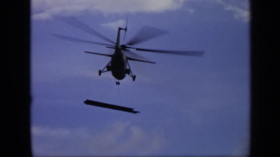 1971 Moscow 8mm frame showing the helicopter larger in frame, with blurred rotors and a long suspended load against blue sky.