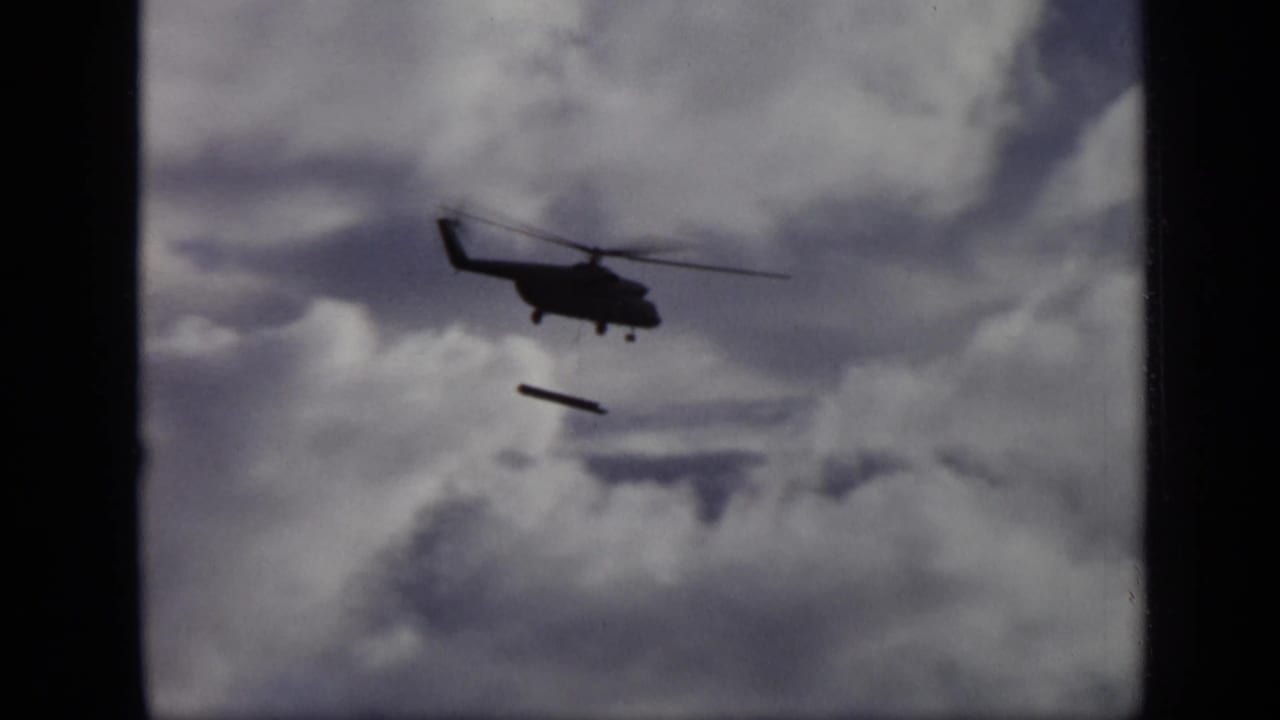 1971 Moscow 8mm frame showing a dark helicopter silhouette with a long object falling below it against thick clouds.