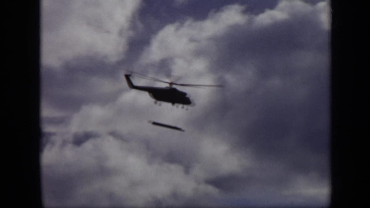 The helicopter remains in silhouette over Moscow metadata, with a narrow object suspended or falling beneath a cloud-filled sky.