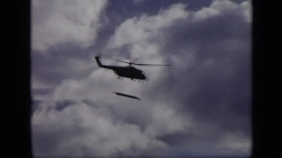 The helicopter remains in silhouette over Moscow metadata, with a narrow object suspended or falling beneath a cloud-filled sky.