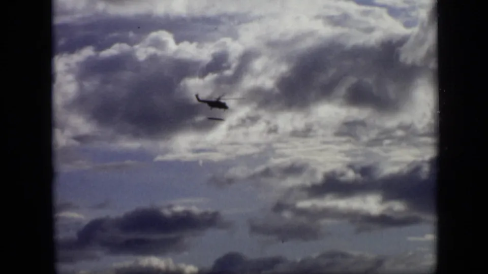 A distant 1971 Moscow helicopter silhouette and small long object are framed low in a broad sky of layered clouds.