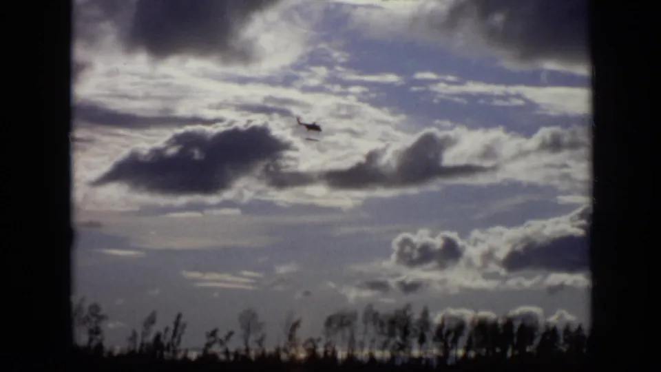 1971 Moscow 8mm frame showing a small helicopter silhouetted against layered clouds above a distant treeline.
