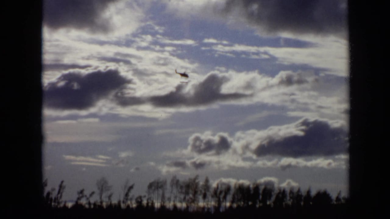 Helicopter in a cloud-filled sky framed by dark vertical borders.