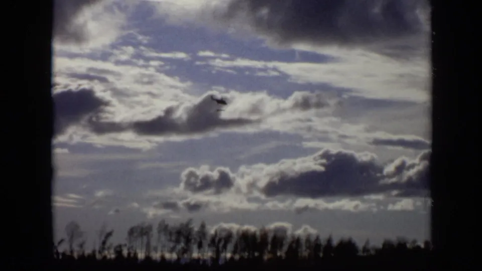 1971 Moscow home-movie frame showing a helicopter near low clouds, with dark trees along the bottom edge.