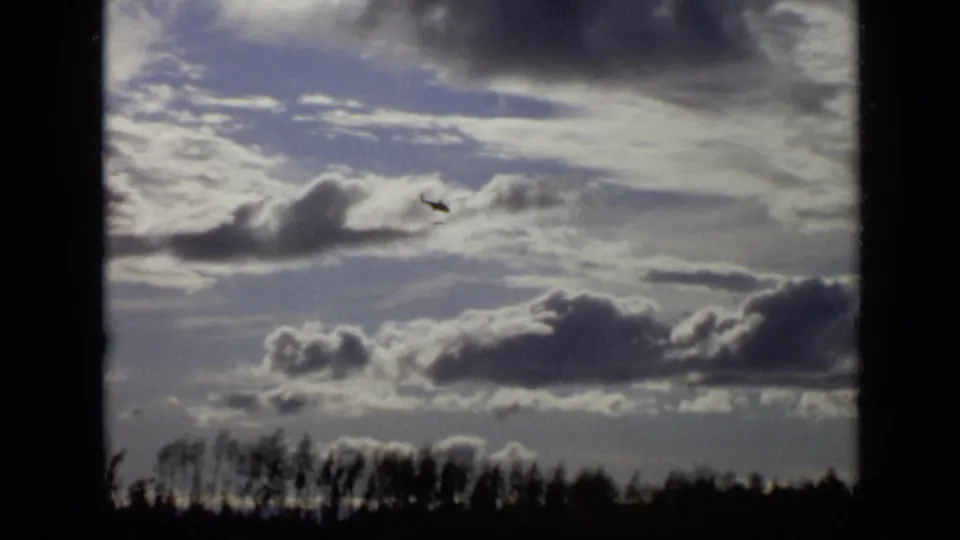 1971 Moscow 8mm frame of a helicopter against textured cloud cover, with a dark treeline at the bottom.